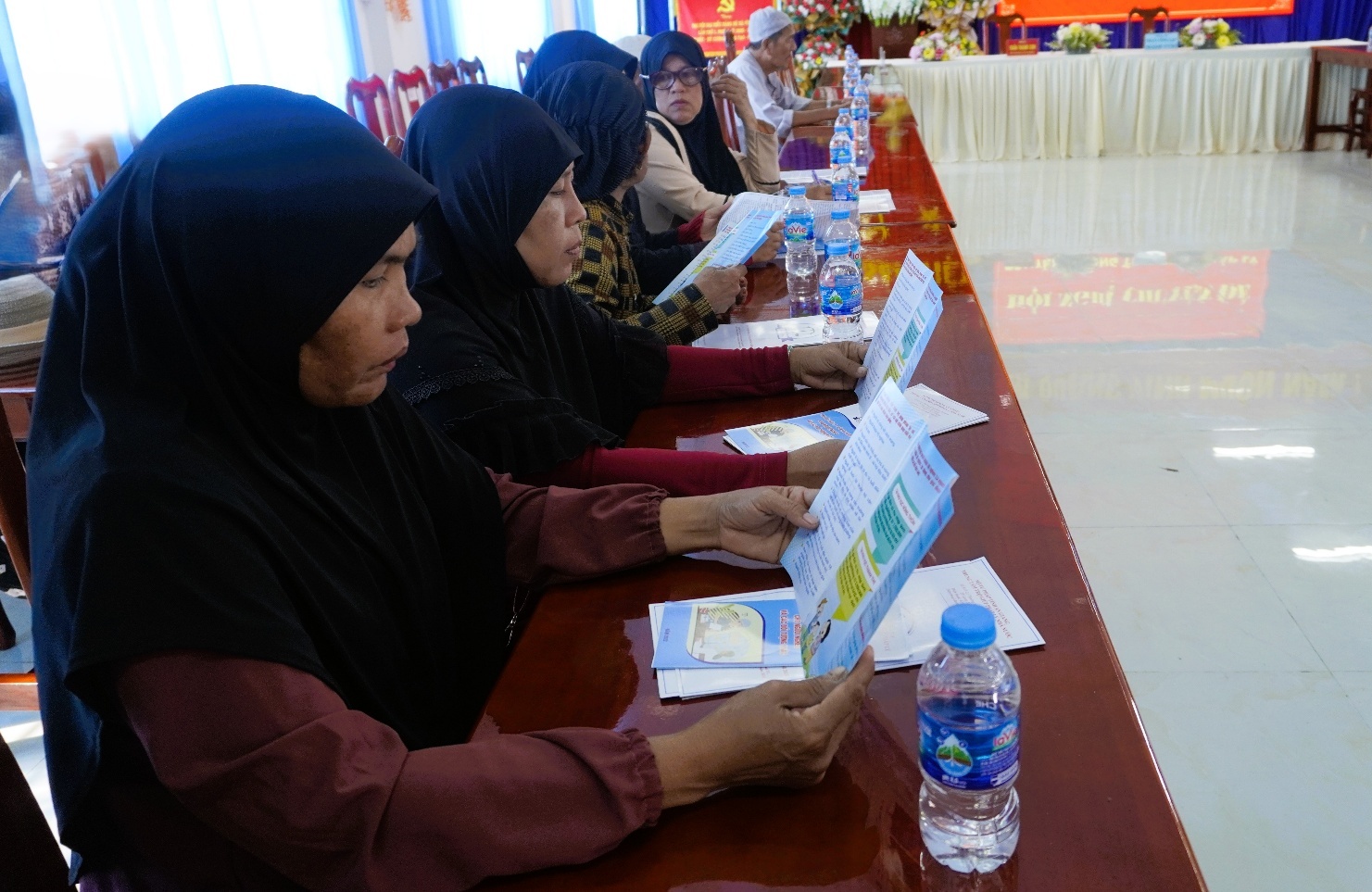 Description: A group of women sitting at a table reading a bookAI-generated content may be incorrect.
